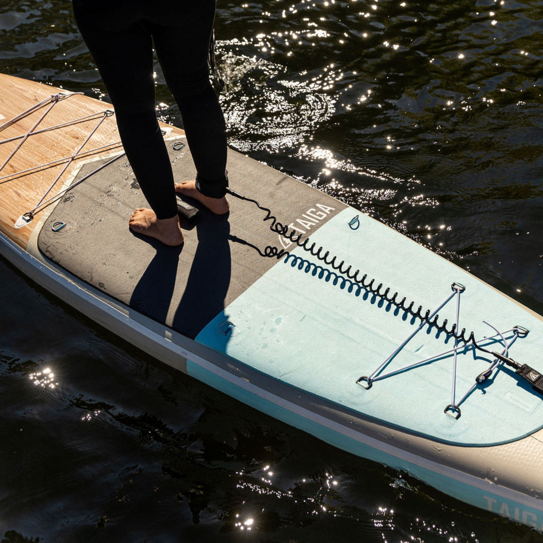 Person standing on a paddleboard with a leash attached, on a body of water.