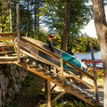 Person loading a paddleboard onto a wooden ramp by a lake with trees in the background