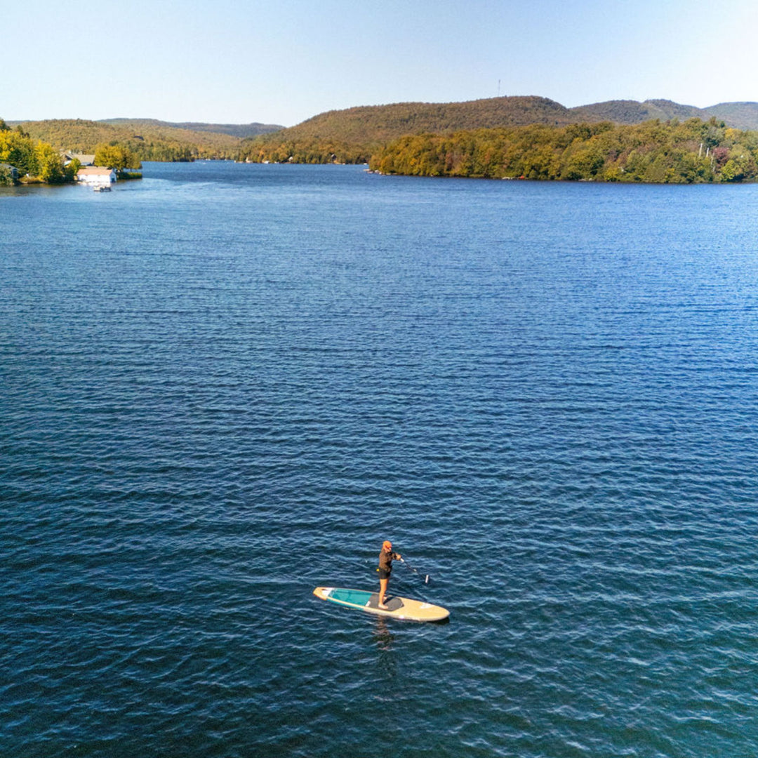 Person paddleboarding on a calm lake with trees and mountains in the background