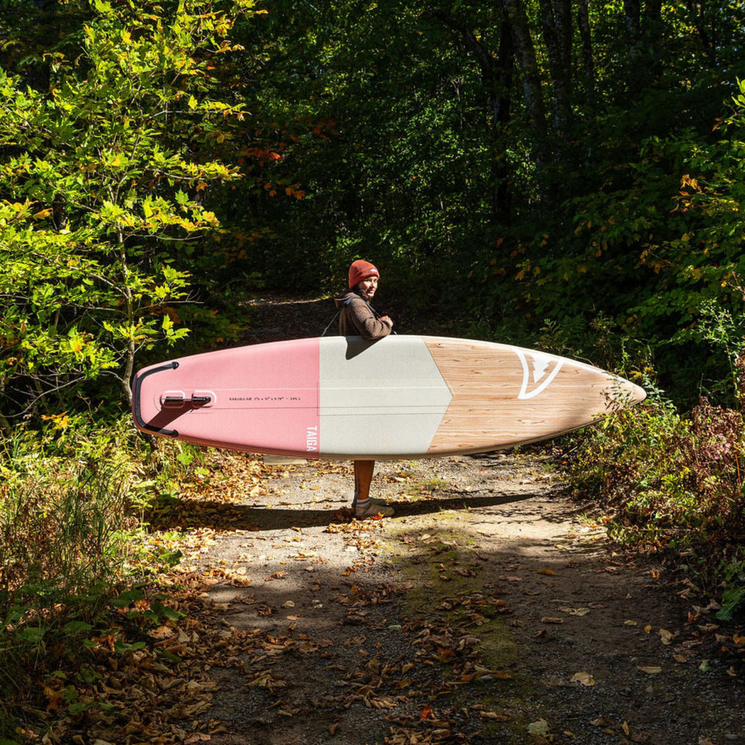Person holding a pink touring paddleboard in a forest