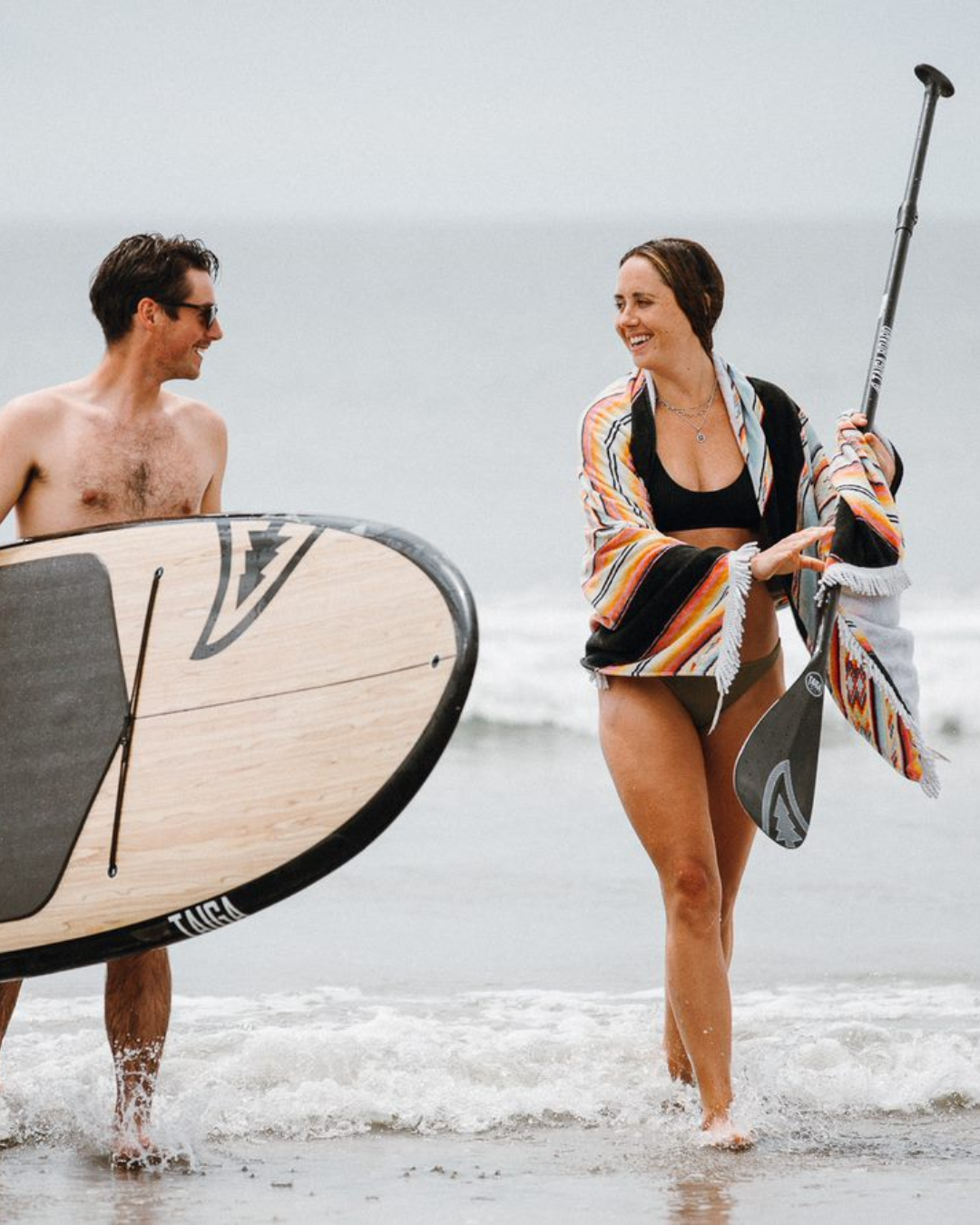 Man and woman with a TAIGA paddle board & paddle on a beach