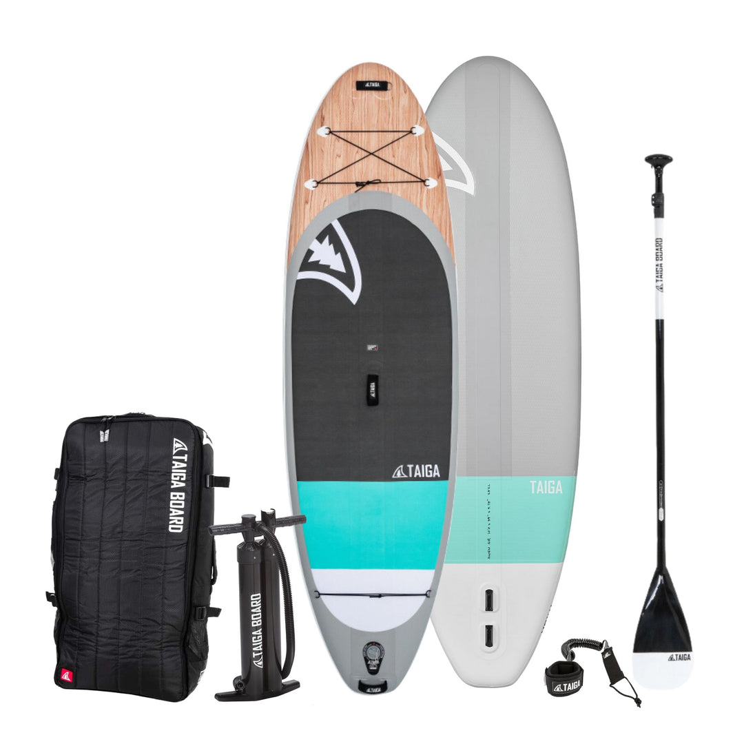 Taiga inflatable stand-up paddle board package including a paddle board, a black Taiga Board Bag, a hand pump, a leash and a paddle on a white background.