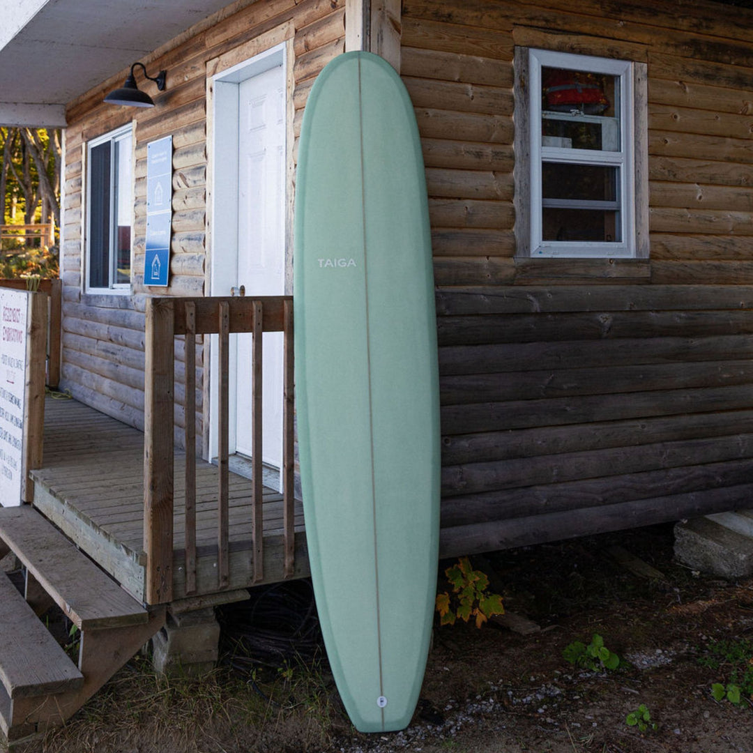 Green surfboard leaning against a wooden cabin