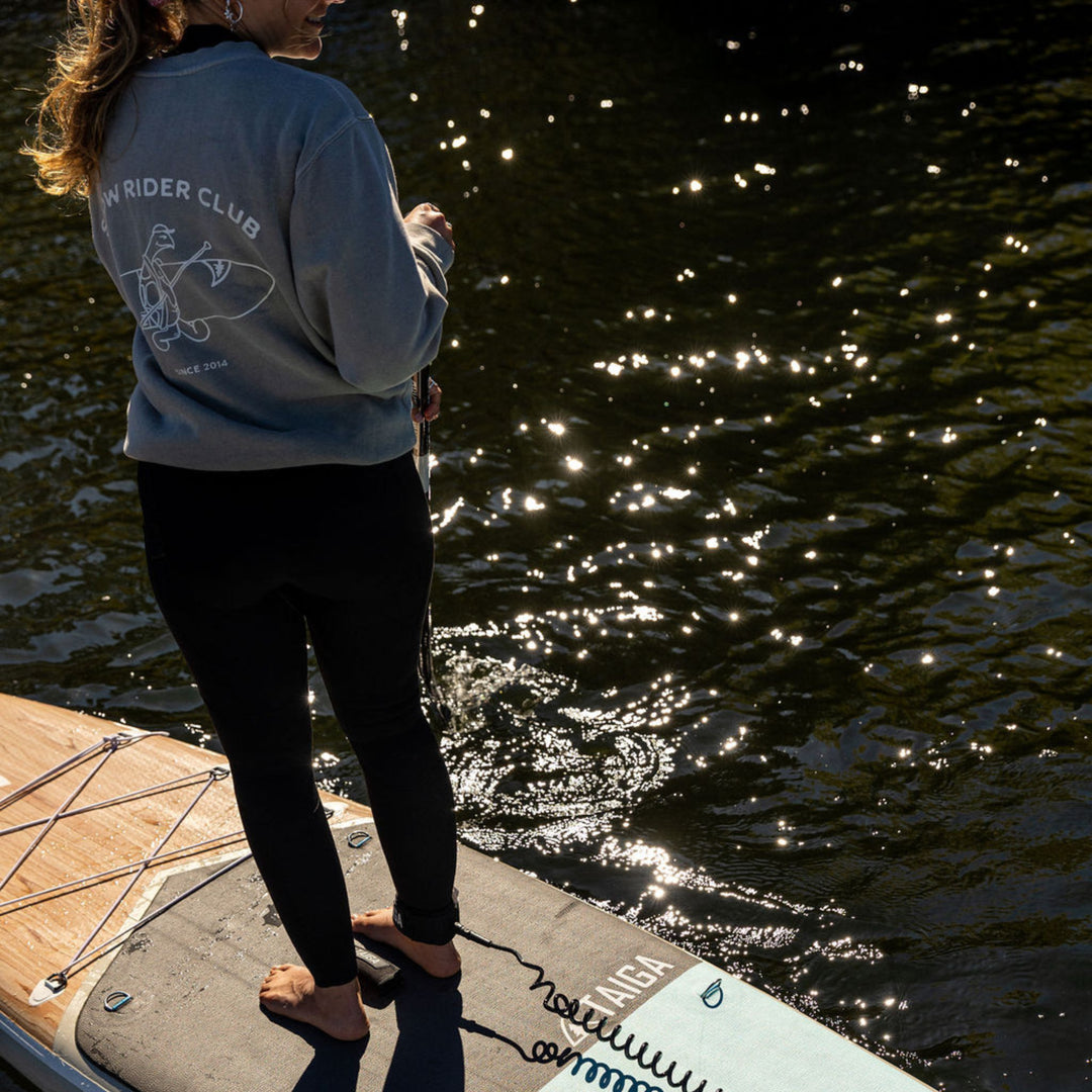 Person standing on a paddleboard, wearing a crewneck with 'Slow Rider Club' text.