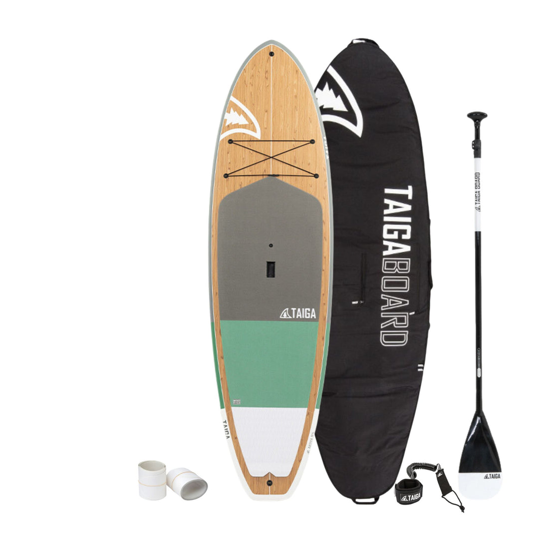 Taiga hard stand-up paddle board set on a white background, including the wooden decked board, black carrying bag, paddle, leash, and rail guards