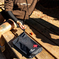 Person sitting on a wooden bench with a black bag featuring a red logo.