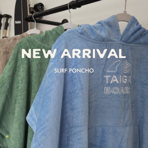 Blue surf poncho with 'Taiga Boards' logo on a rack with green poncho, text 'New Arrival Surf Poncho'.