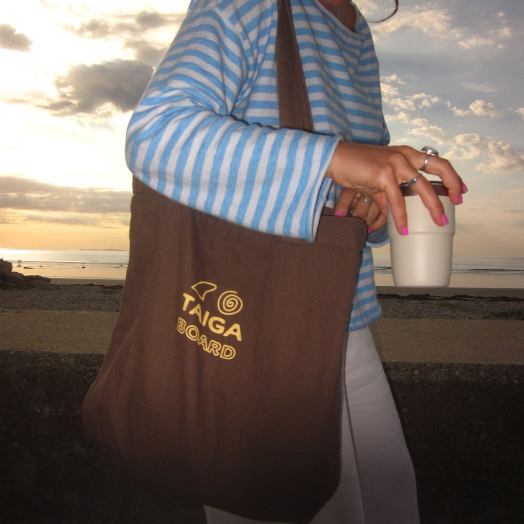 Person holding a tote bag & a coffee with a scenic beach background