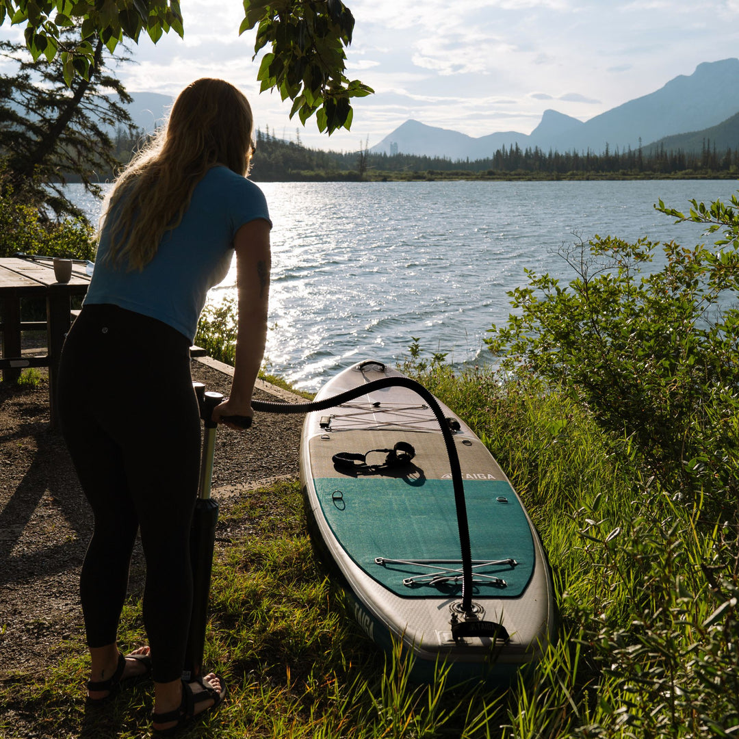Woman inflating a paddleboard by a lake with mountains in the background