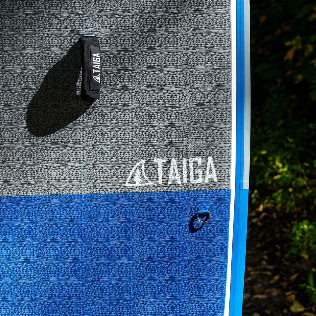Close-up of a gray and blue paddle board mat with 'TAIGA' branding.