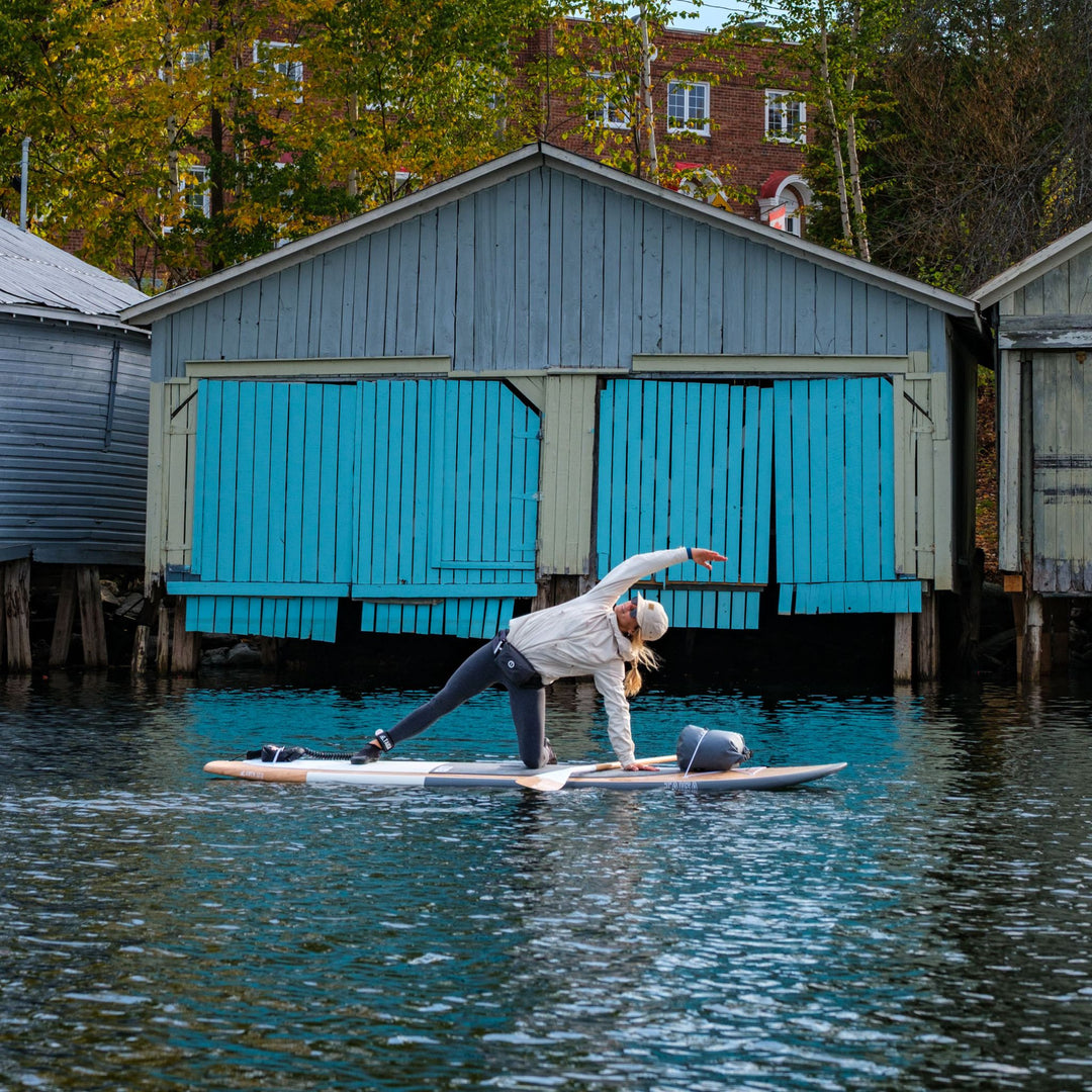 Girl doing yoga on a on a hard wooden SUP near boat houses in fall