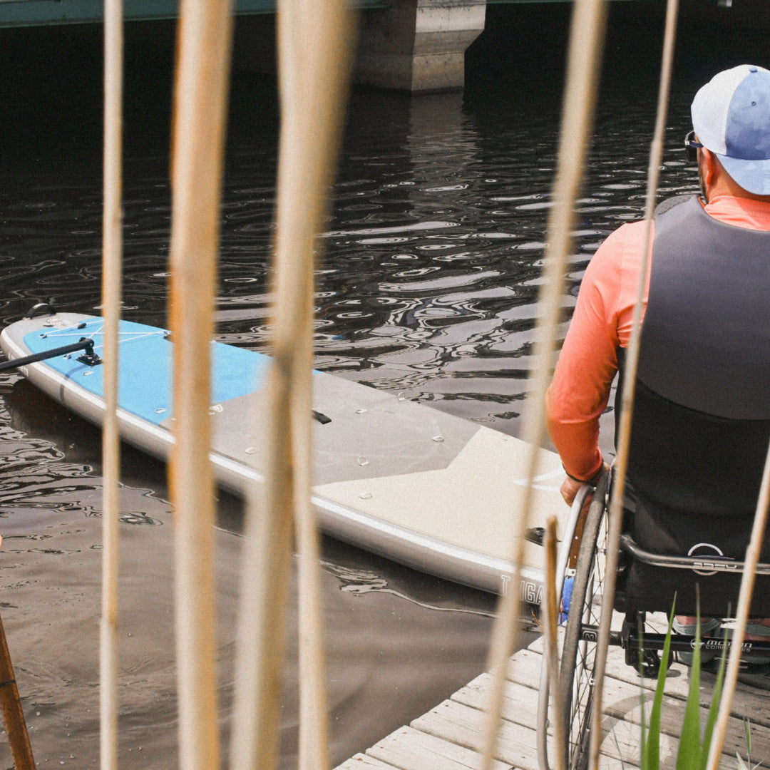 Person in a wheelchair by a dock with a paddleboard