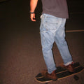 Person standing on a skateboard wearing blue jeans and brown shoes in a dark setting